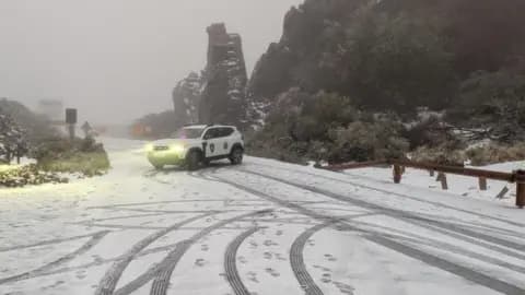 An emergency services car parked across a snow-covered rural road in fog