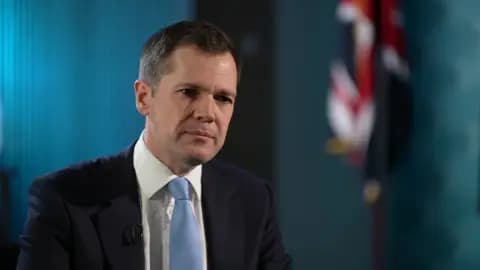 Jenrick wears a suit and a light blue tie as he looks at a person off-camera.