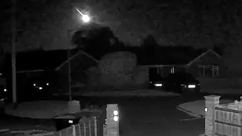 A doorbell camera image at night with a bright meteor flying across the sky.