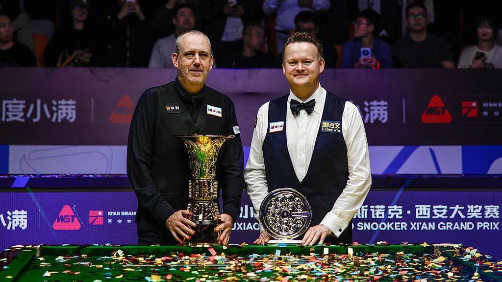 Mark Williams and Shaun Murphy stand next to a snooker table with their trophies, surrounded by colourful tape
