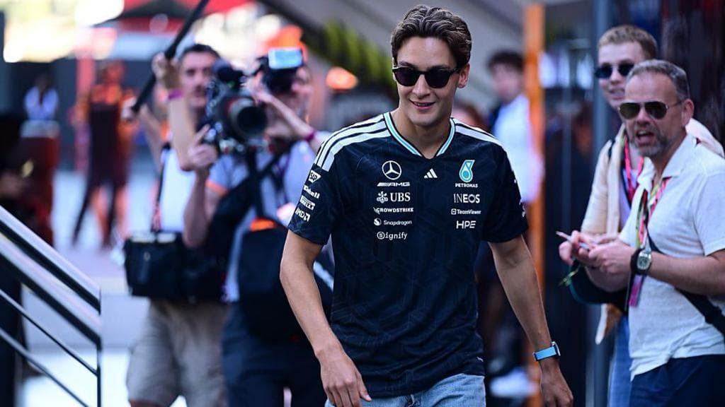 George Russell, wearing sunglasses, walks through the paddock at the Barcelona-Catalunya Grand Prix