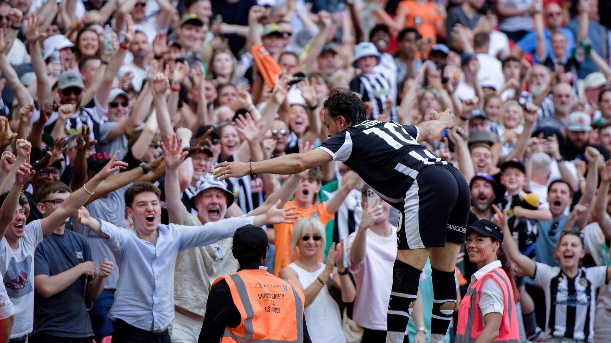 Jodi Jones jumps on to the advertising boards to celebrate with Notts County fans after he scored against Salford City at Wembley