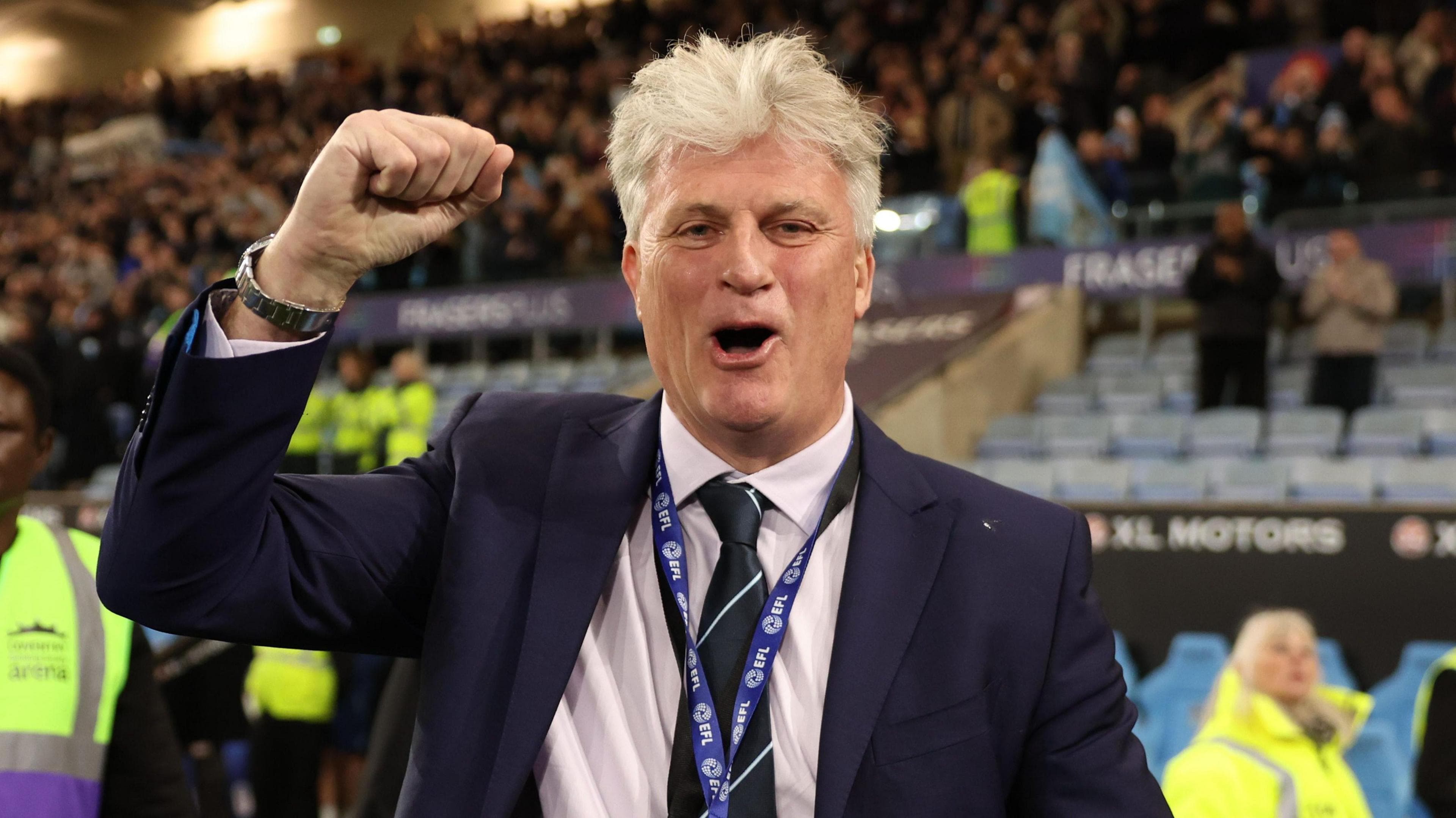Doug King clenches his fist in celebration wearing a suit after Coventry's title-sealing win over Portsmouth on Tuesday
