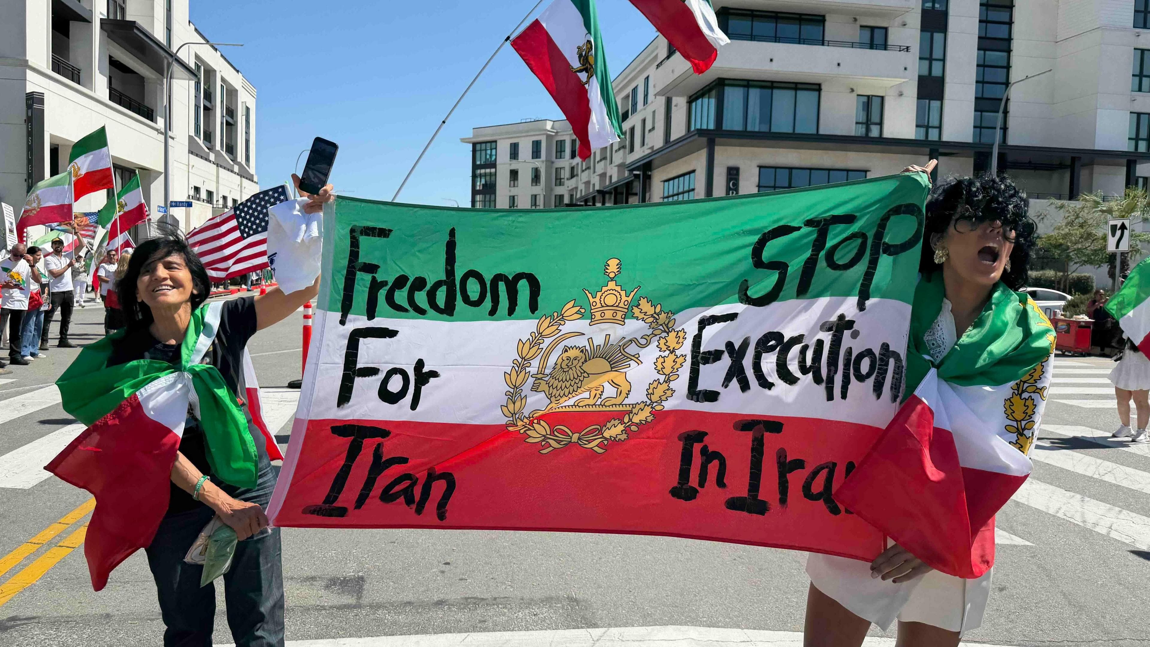 Two female protesters hold Iran's pre-1979 Islamic revolution flag, which has "Freedom for Iran" and "Stop execution in Iran" written on it in large black letters.