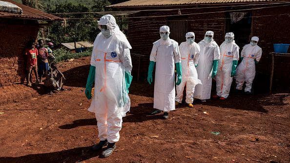 Health workers wearing white protective equipment stand during safe burial procedures outside a family home in the community of Mongbwaluon in the Democratic Republic of Congo.