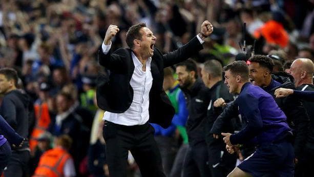 Frank Lampard celebrates on the touchline wearing a black suit and white shirt with fists clenches above his head
